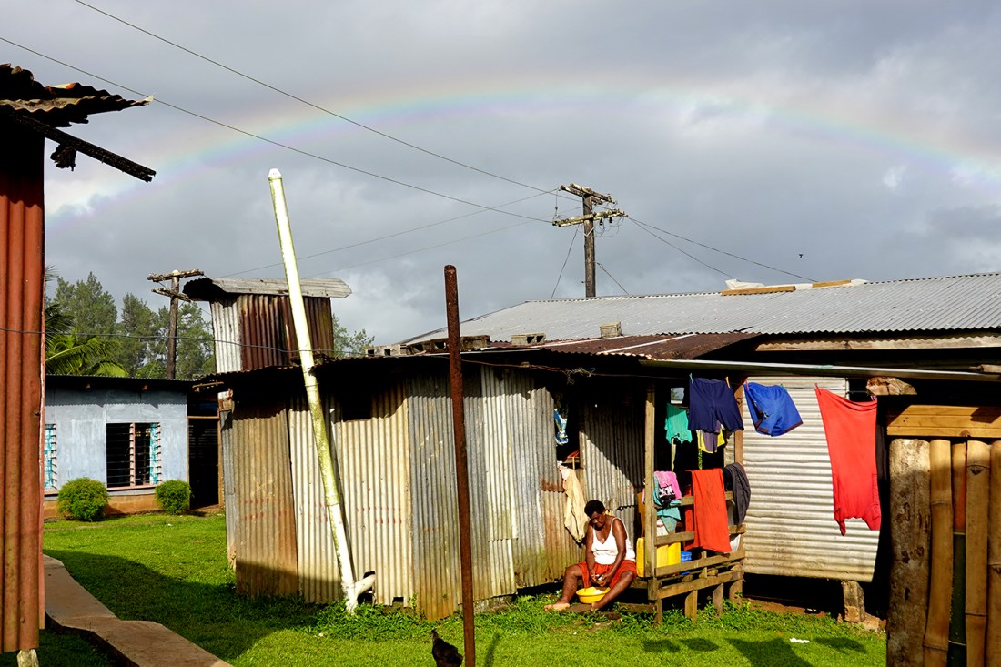 A village scene with tin-roof homes and a rainbow in the sky in Fiji.
