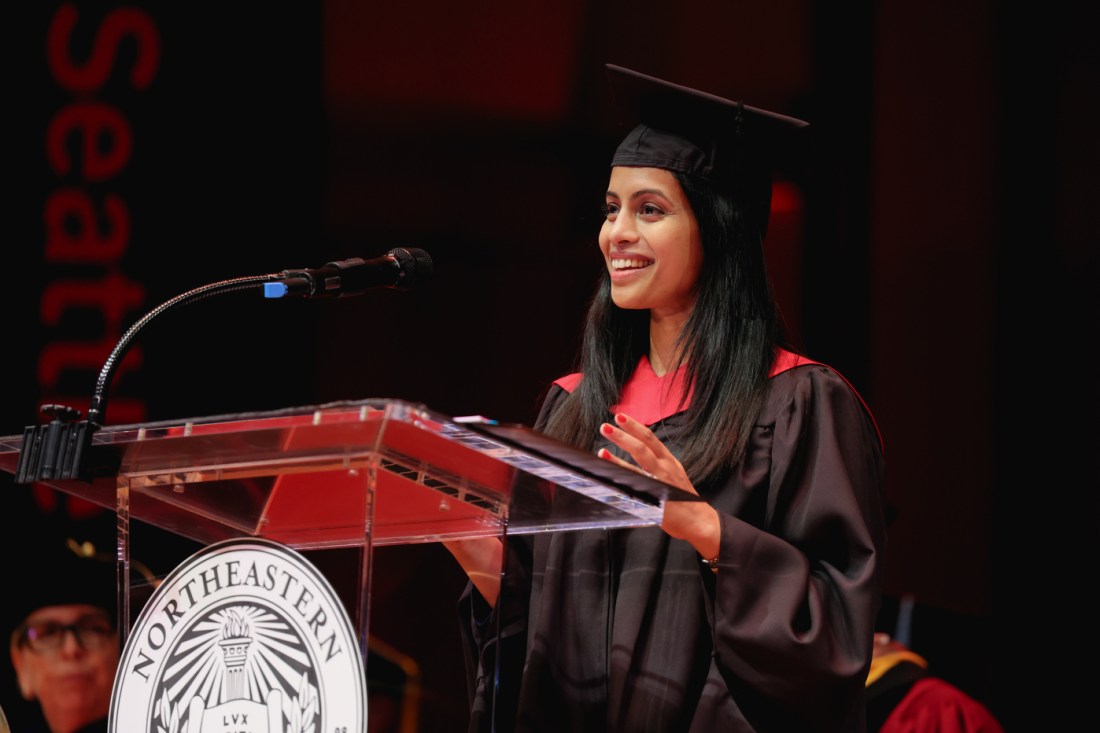 A smiling graduate speaks at a podium in front of a microphone during the Seattle Campus Commencement Ceremony.
