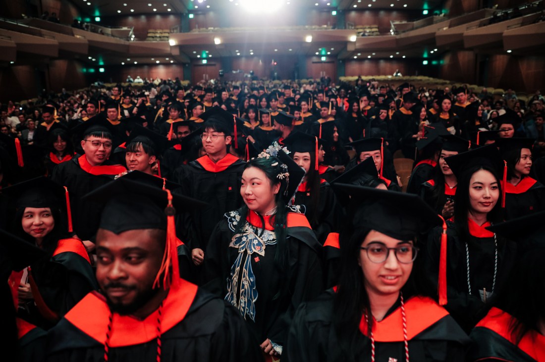 Rows of Northeastern graduates wearing black caps and gowns with red accents seated inside of Benaroya Hall for the Seattle Campus Commencement Ceremony.