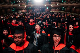 Rows of Northeastern graduates wearing black caps and gowns with red accents seated inside of Benaroya Hall for the Seattle Campus Commencement Ceremony.