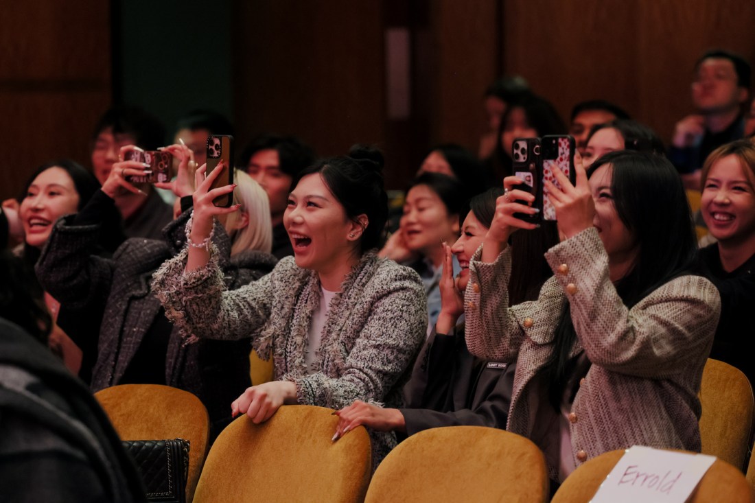 A group of audience members laugh and take photos with their phones from their seats during the Seattle Campus Commencement Ceremony at Benaroya Hall.