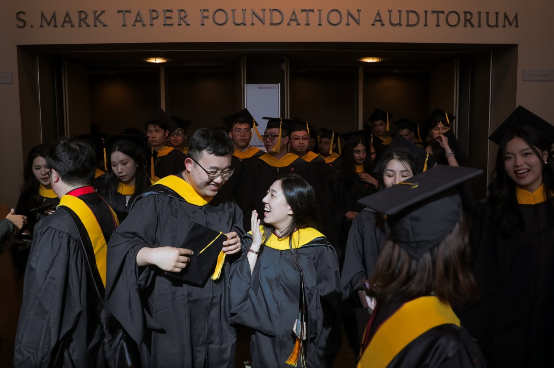 Two graduates smiling and laughing with each other at the front of a crowd of graduates exiting Benaroya Hall from the Seattle Campus Commencement ceremony.