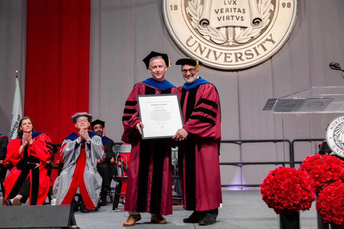 Stephen Lynch on stage, holding a large framed document.