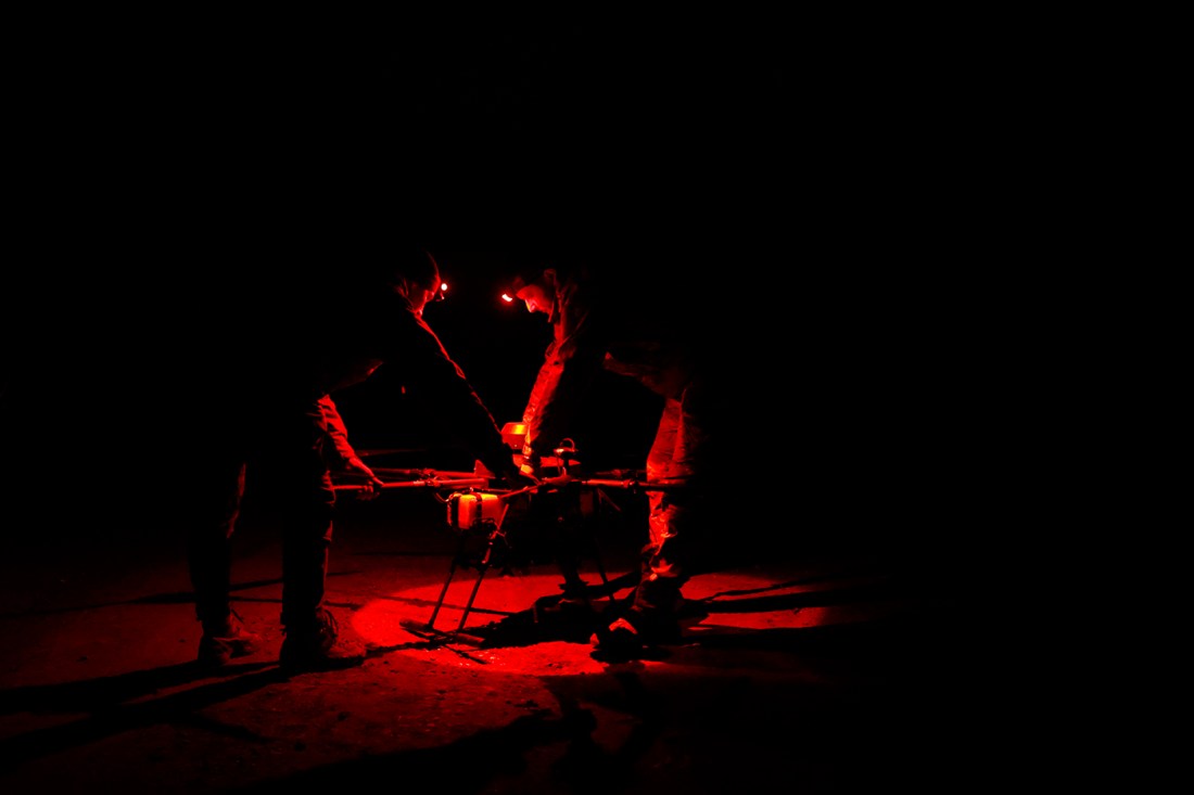 Two military men examine a drone, which is illuminated red.
