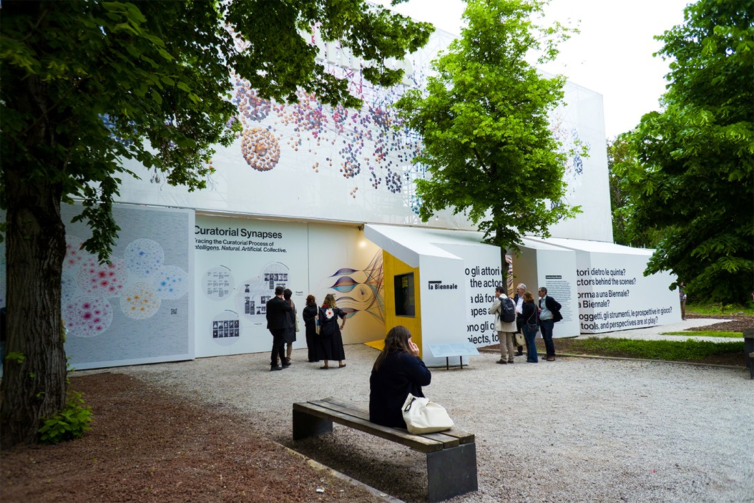 People standing and sitting outside by an ehibit at the Venice Biennale.