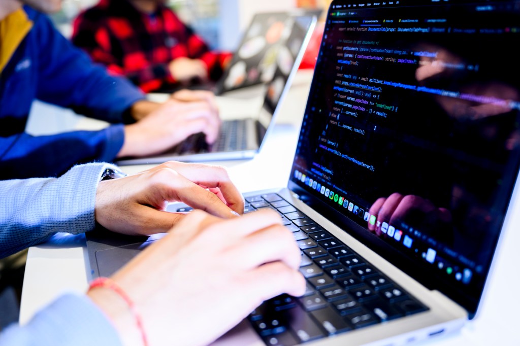 The hands of two people sitting at two different laptops typing next to each other.