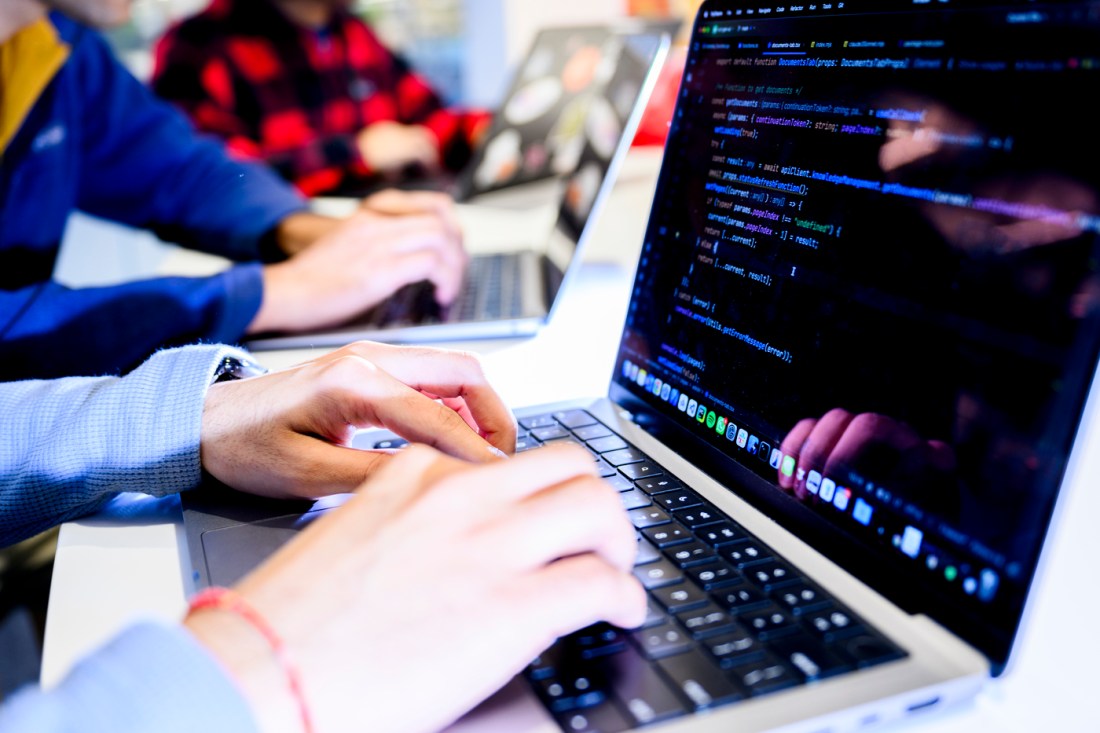 The hands of two people sitting at two different laptops typing next to each other.