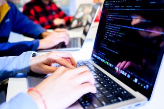 The hands of two people sitting at two different laptops typing next to each other.