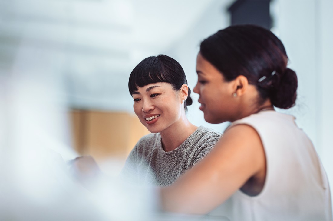Two professional women engaged in a collaborative discussion in a modern office setting.