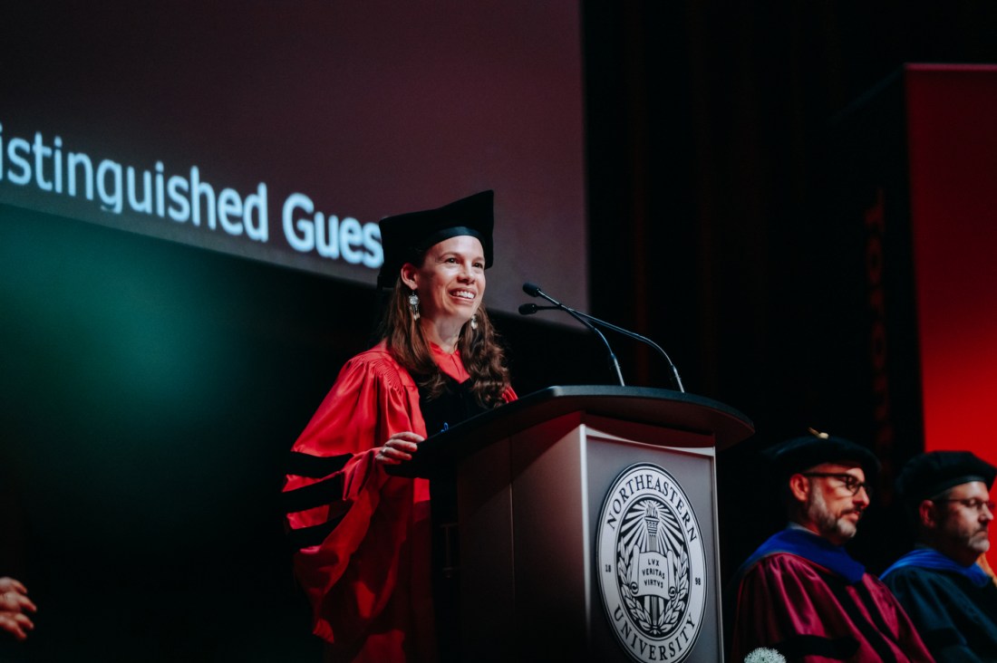 A person wearing red and black regalia and a commencement cap stands at a podium at Meridian Hall in Toronto.