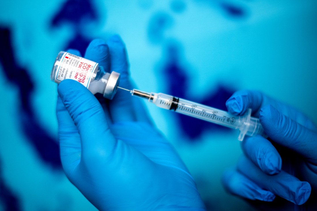 Close-up of gloved hands drawing a COVID-19 vaccine dose from a vial with a syringe.