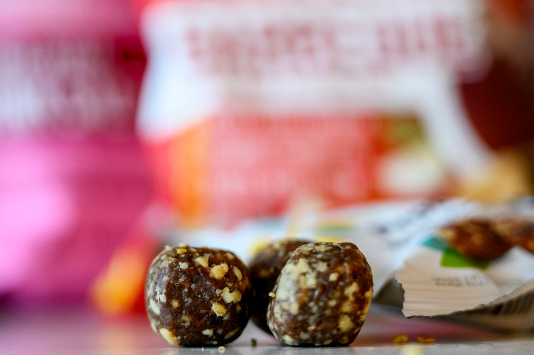 Three energy ball snacks made of dates and nuts laid out on a surface next to an open package.