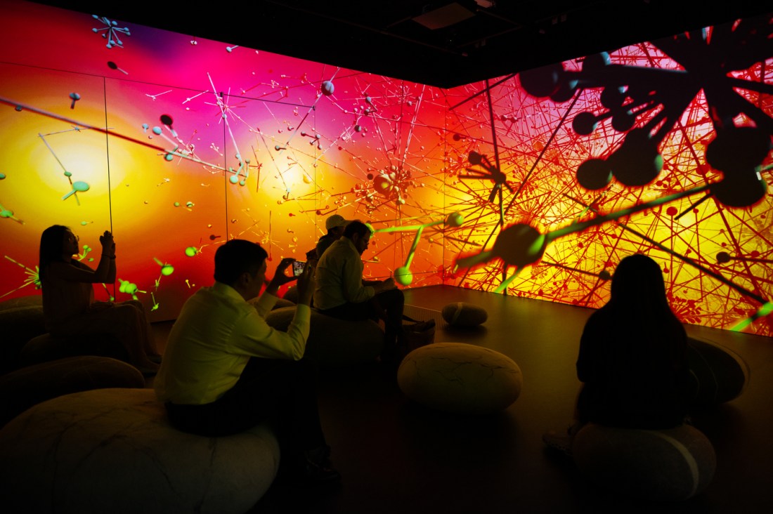 People sit in a dark room surrounded by colorful, abstract visuals projected on the walls.