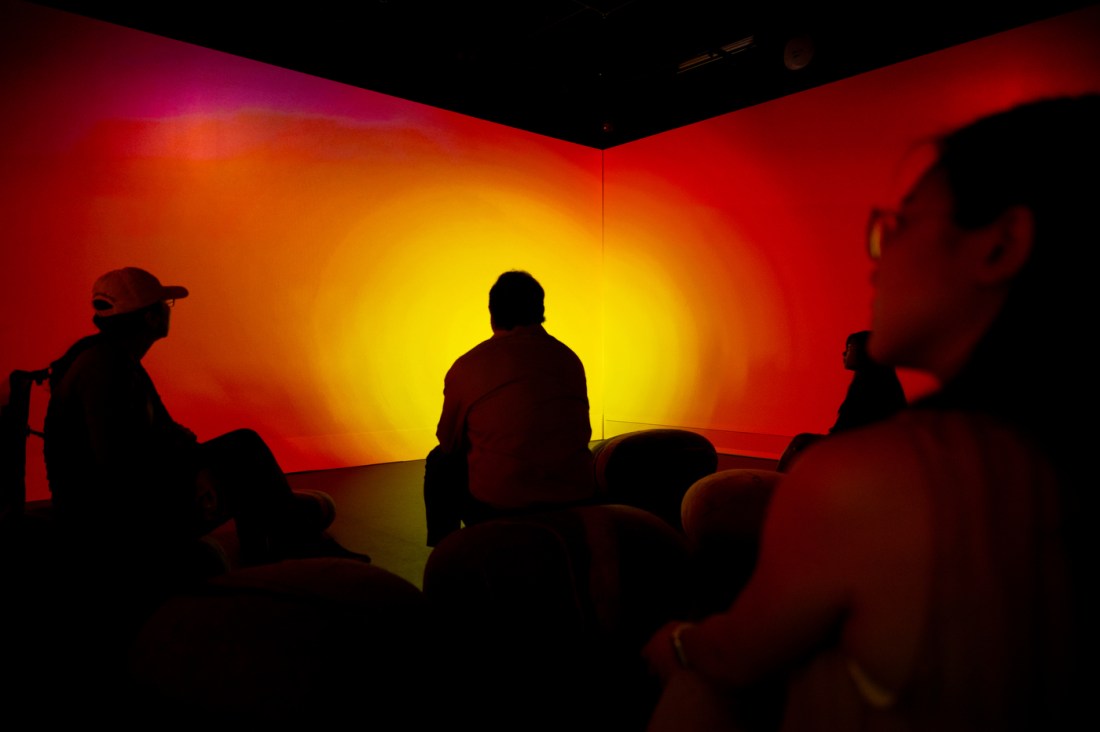 Silhouettes of people sit in a glowing red-orange room, surrounded by abstract immersive visuals.