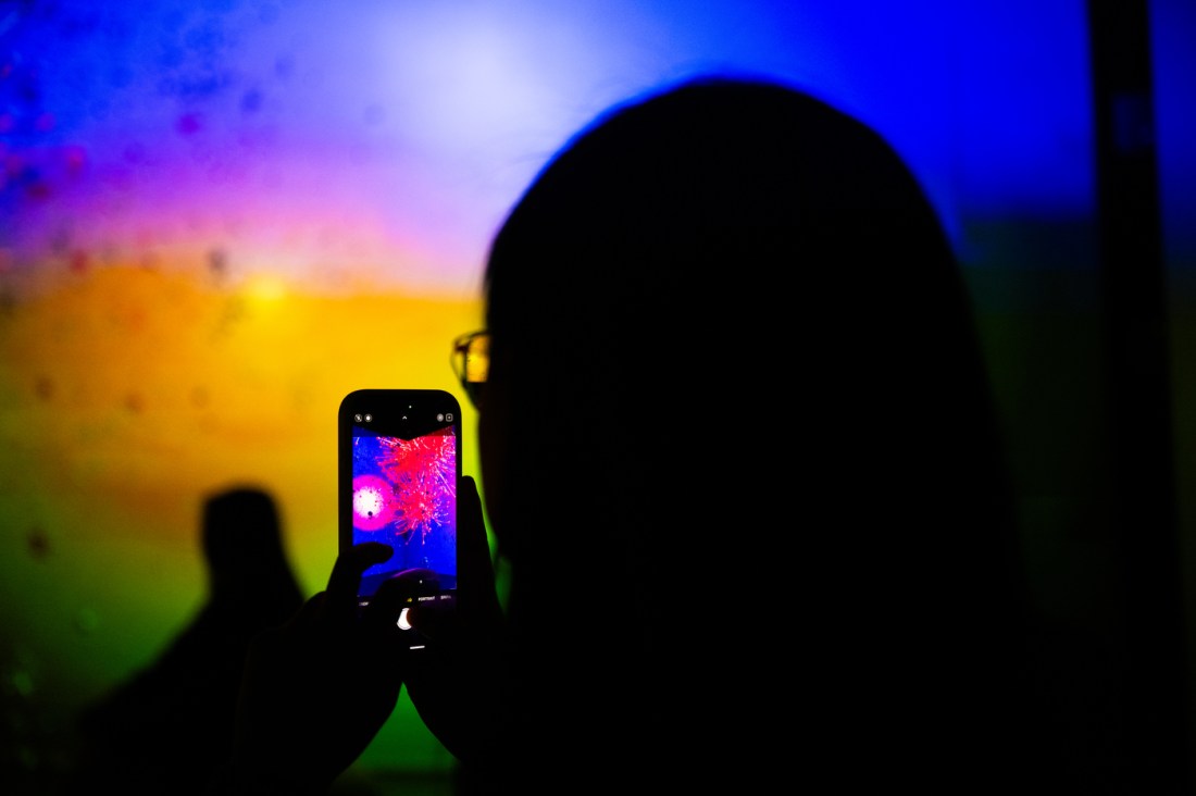A visitor records a data-driven art exhibit about COVID misinformation inside a glowing multi-colored room.