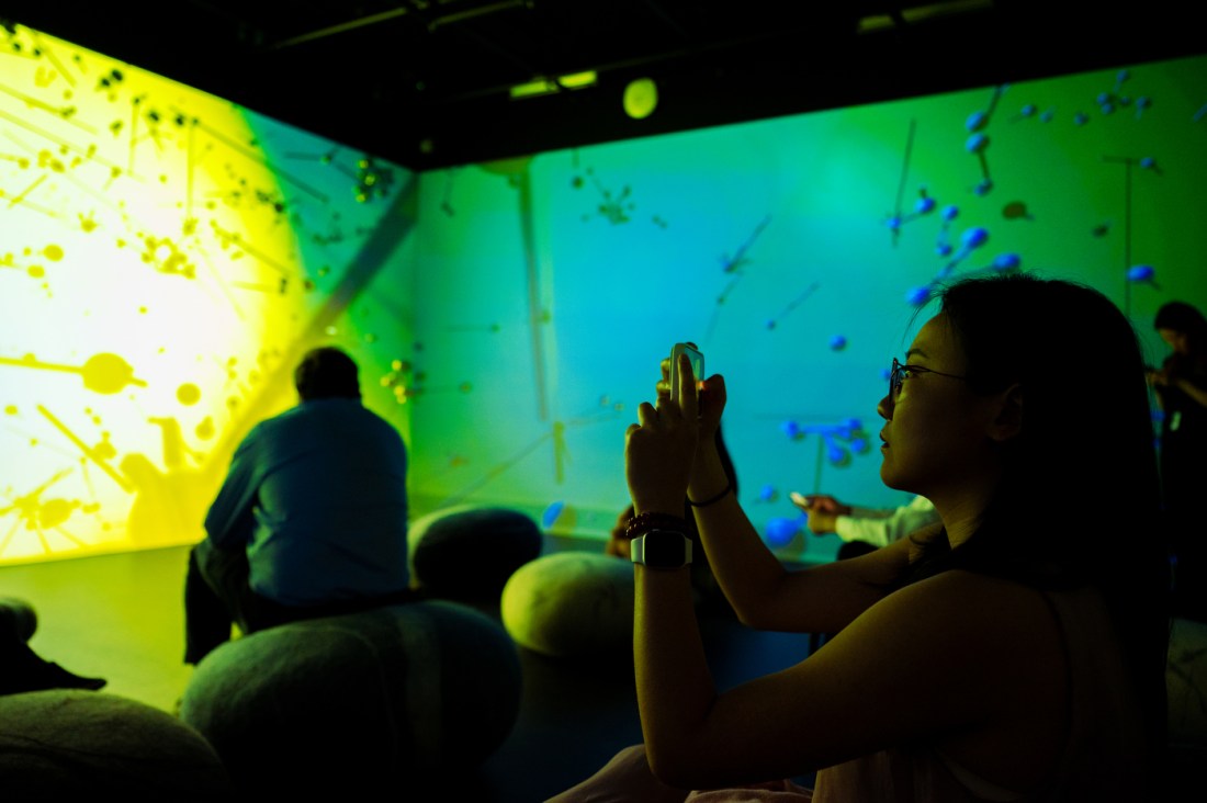 Visitors interact with a digital art projection filled with bright green and yellow visuals at an immersive gallery event.