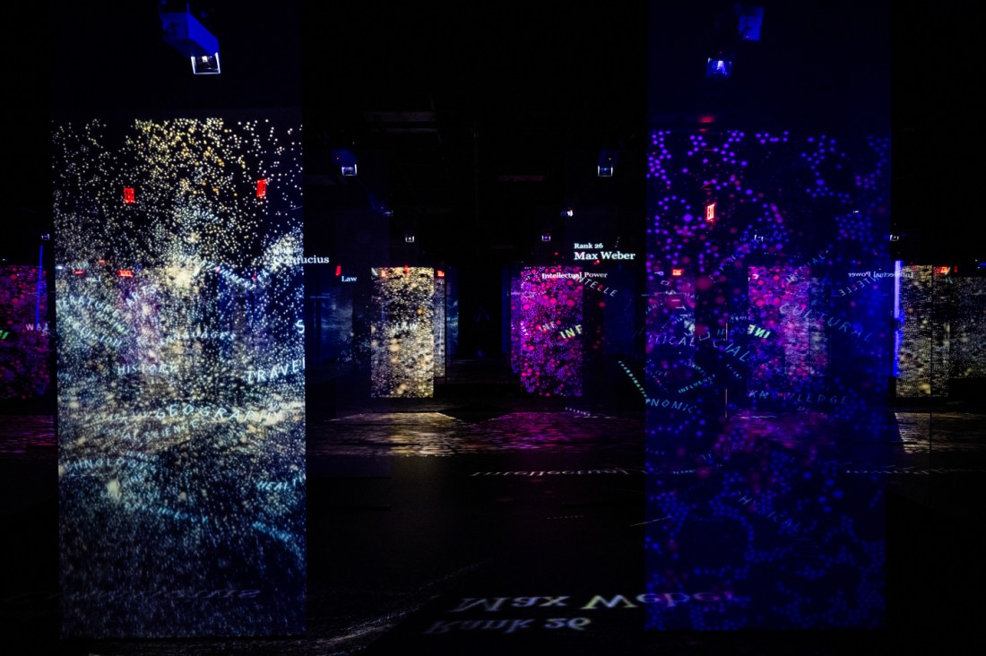 Abstract immersive art panels display swirling constellations of names, words, and networks in a dark exhibition space.