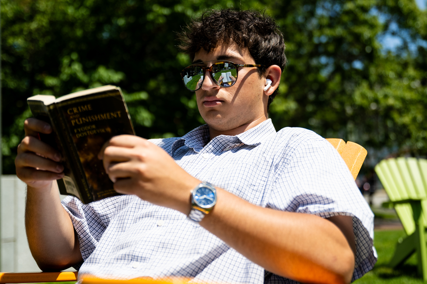 A person reads a book while sitting outdoors in the sunlight.