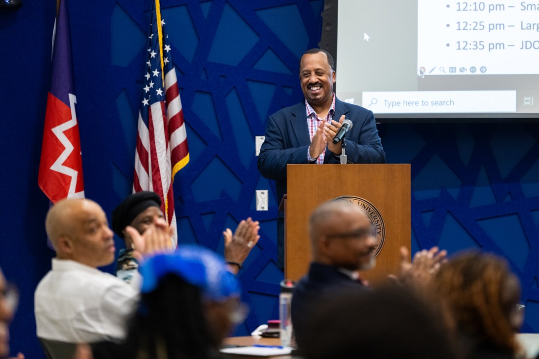 Juneteenth campus event features speaker in front of U.S. and university flags.