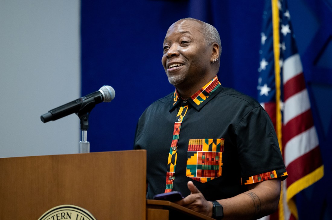 A speaker stands at a podium, smiling while addressing an audience.