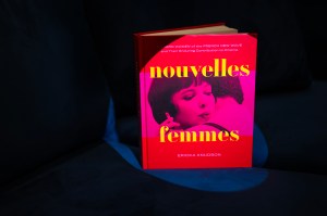 The brightly-colored book "Nouvelles Femmes" standing upright on a dark chair on a black background.