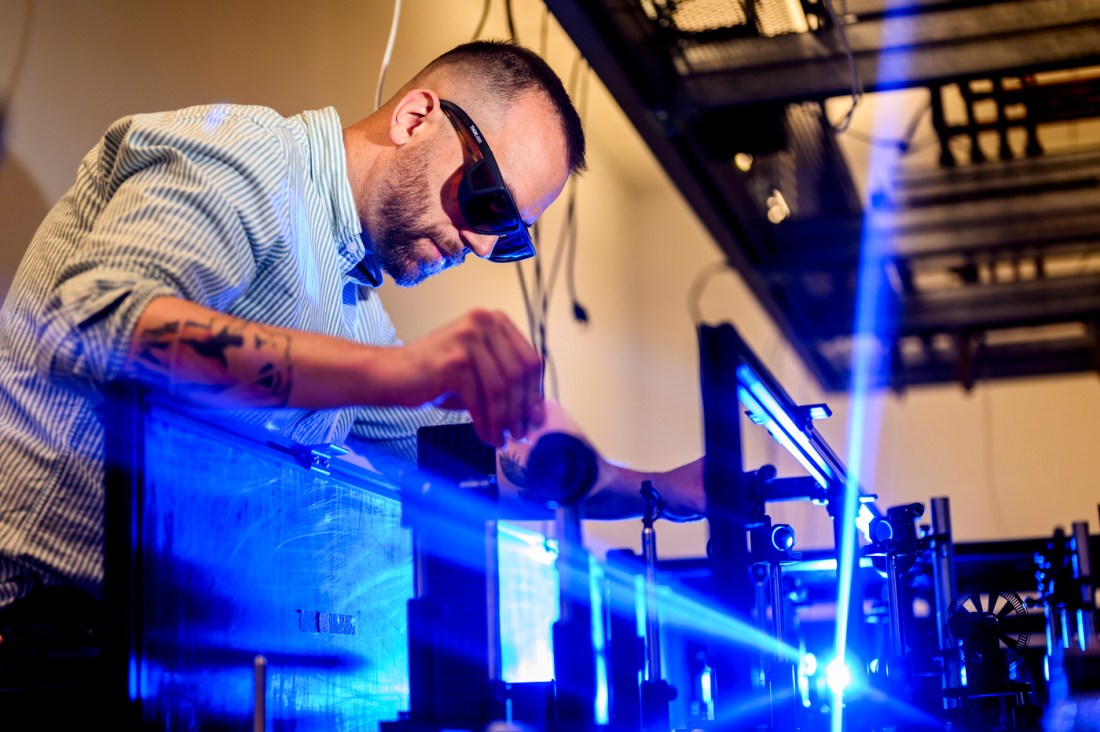 Researcher wearing protective glasses adjusts equipment while working with blue laser beams in a quantum optics lab.