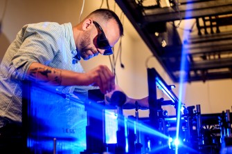 Researcher wearing protective glasses adjusts equipment while working with blue laser beams in a quantum optics lab.