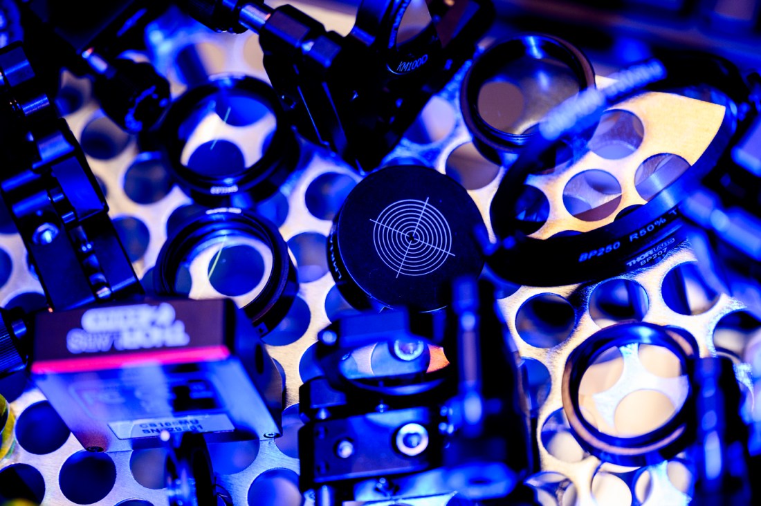 Array of optical components and mounts illuminated by blue and purple lighting.