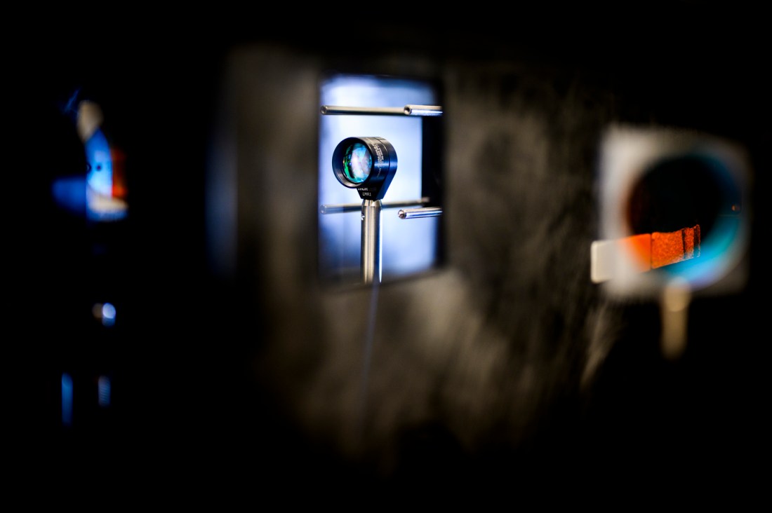 Close-up of a laser setup reflecting light through a circular lens in a dark lab.