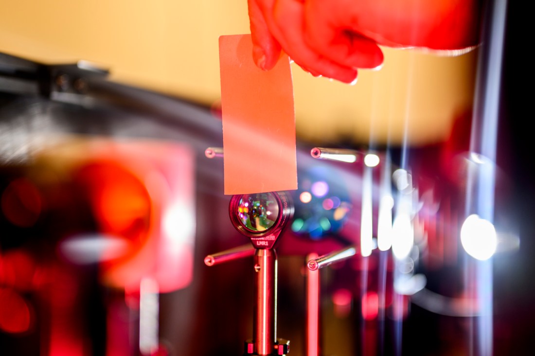Hand holds a translucent card in front of scientific equipment, lit by red lasers.