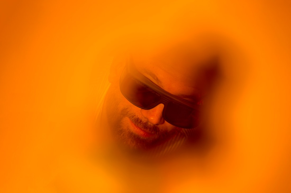 Researcher wearing dark glasses appears through an orange glow during an experiment.