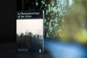 Book cover of 'A Phenomenology of the Alien' in front of an atmospheric, blurred landscape with trees.