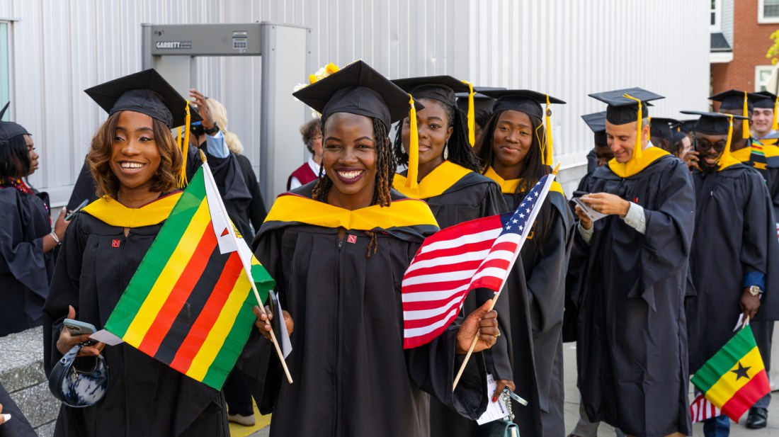 Graduates holding flags smile outside the venue at the Northeastern commencement in Portland.