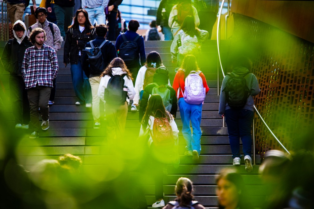 People walk up and down a staircase on a campus framed by greenery.