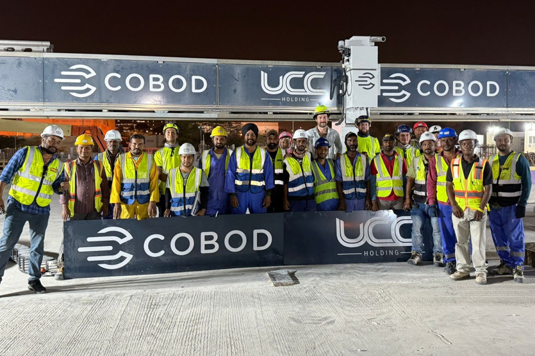 Construction crew in Qatar stands in front of one of the largest 3D printers in the world, built by COBOD and UCC Holding.