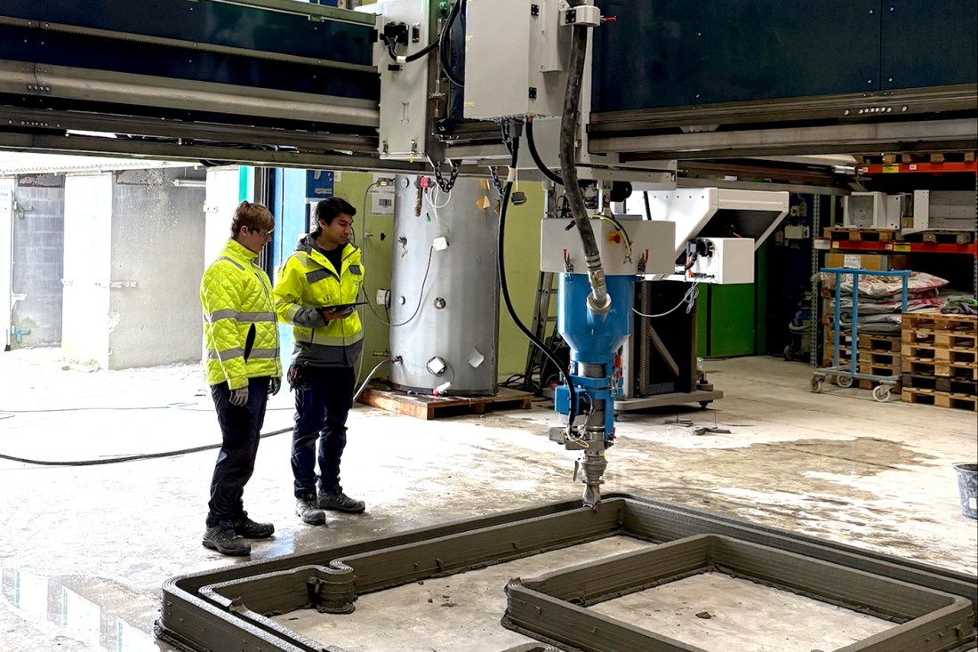 Engineers operate one of the largest 3D printers during a live print demo, showcasing the machine’s construction capabilities indoors.