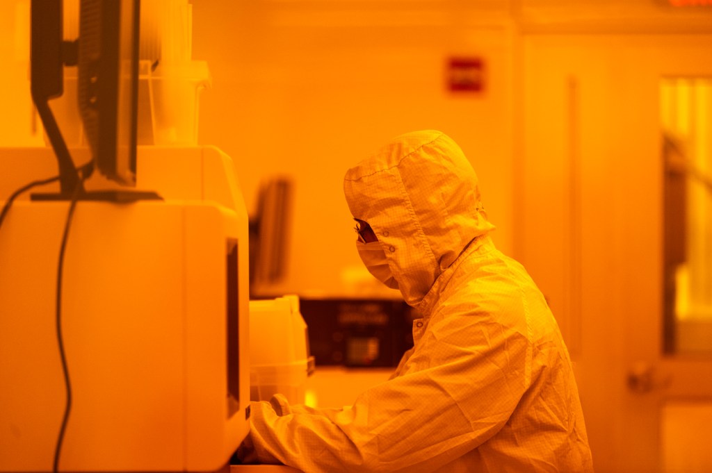 A person in protective gear works with equipment in a brightly lit lab.