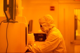 A person in protective gear works with equipment in a brightly lit lab.
