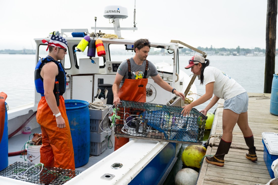 Three people loading crates of lobsters off of a lobster boat in Portland.