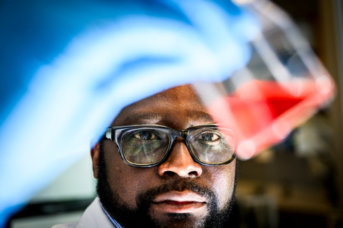 Fleury Augustin Nsole Biteghe holds up a beaker of a red colored liquid in a lab.