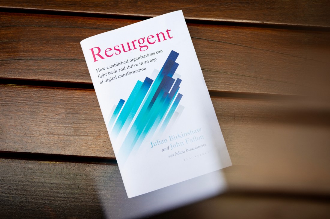 A copy of 'Resurgent' by John Fallon lying on a wooden surface, showing a blue geometric design on a white cover.