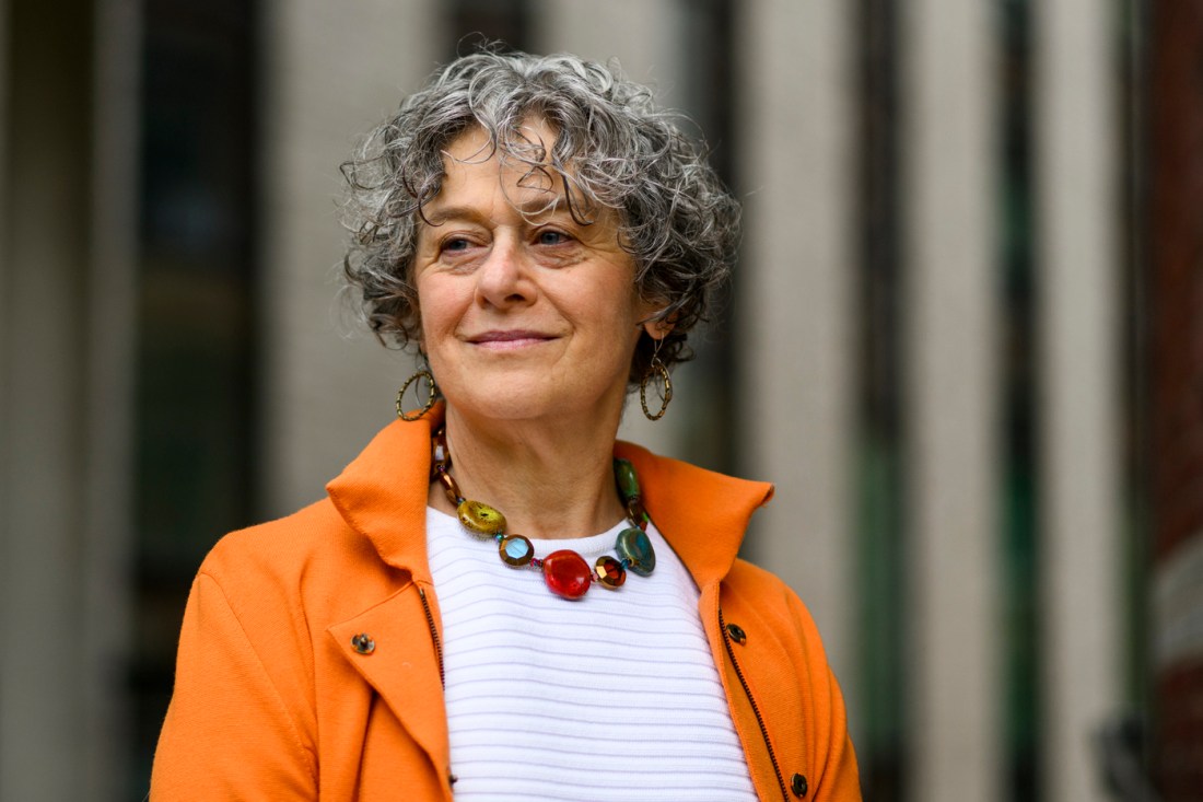 Rose Zoltek-Jick, Northeastern law professor and civil rights project director, poses outdoors in an orange blazer over a white top, wearing a colorful beaded necklace and hoop earrings, with short curly gray hair. She stands against a blurred urban background. Photo by Matthew Modoono/Northeastern University.