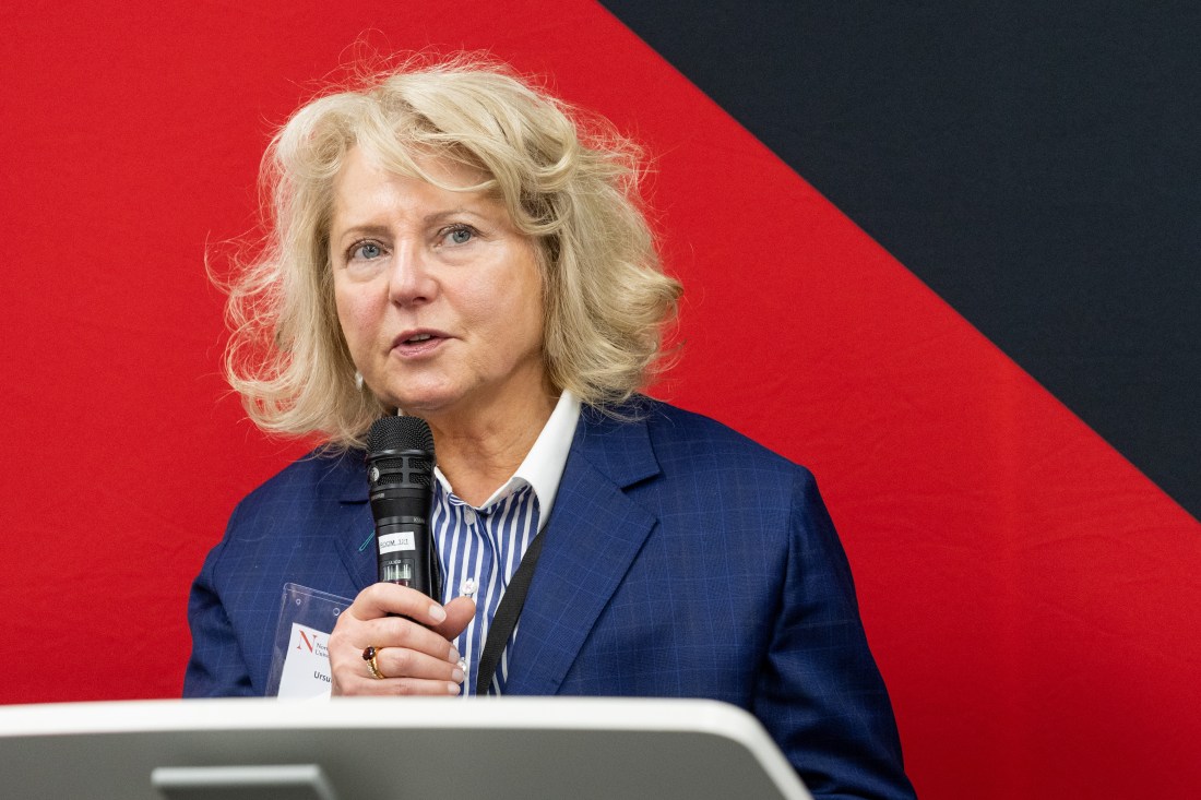 Portrait of Ursula Smartt standing at a podium speaking into a microphone.