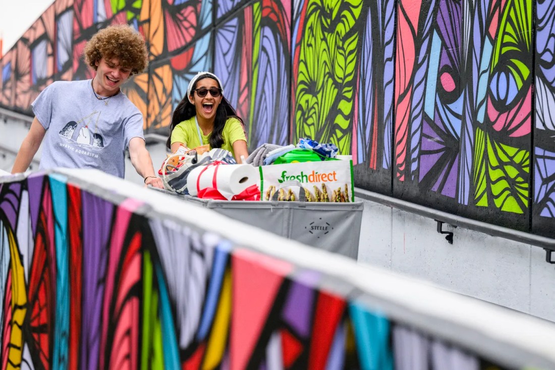 People walk down the ramp in front of the 100 Years of Solitude mural with a cart full of things for their dorm