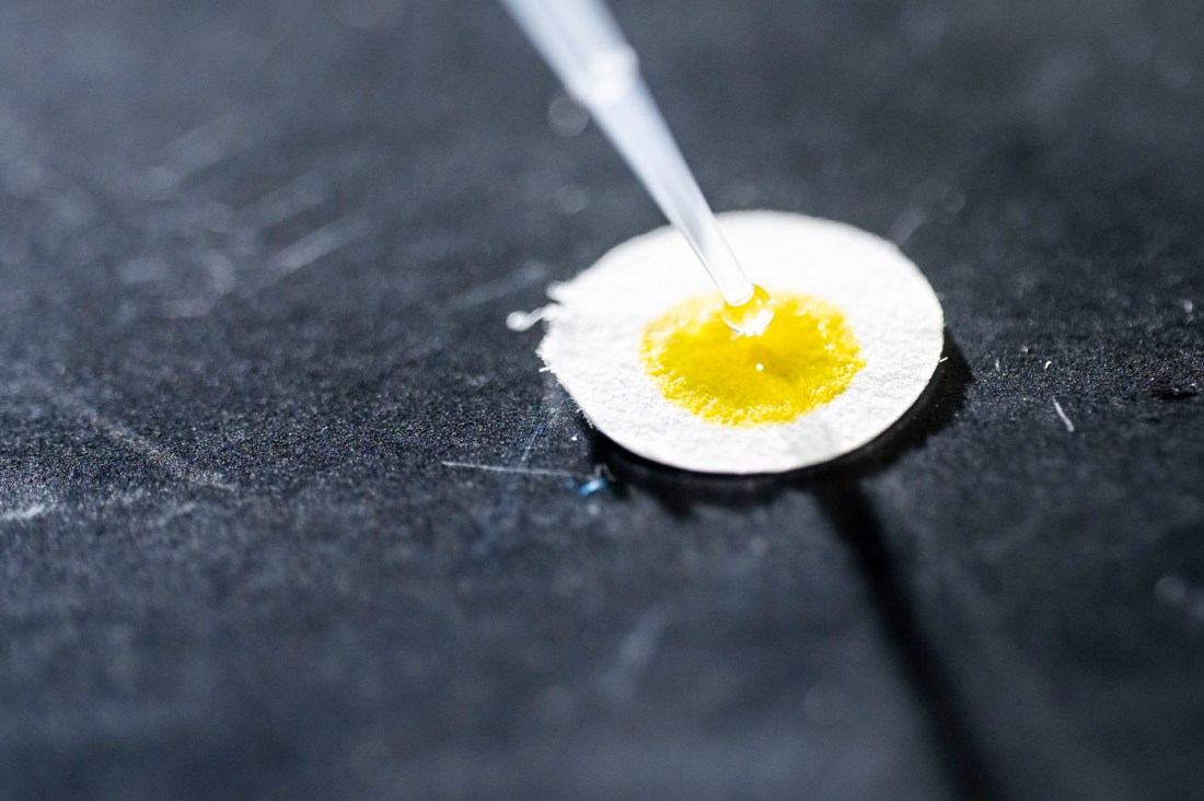 A pipette hovering over a yellow lab test sample. 