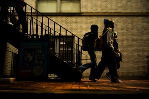 Students walking across campus at sunset, silhouetted against a brick building and stairway.