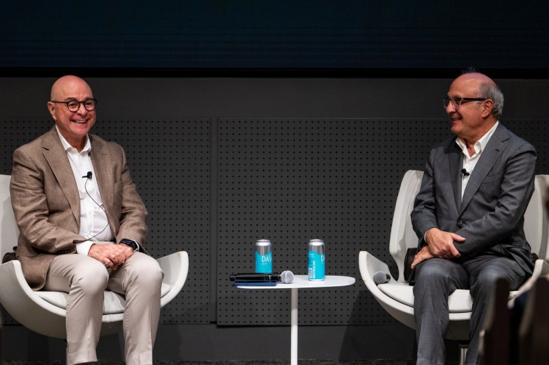 Two men sit in armchairs on stage, smiling as they converse during a fireside chat at Northeastern University’s Senior Leadership Retreat in the ISEC auditorium.