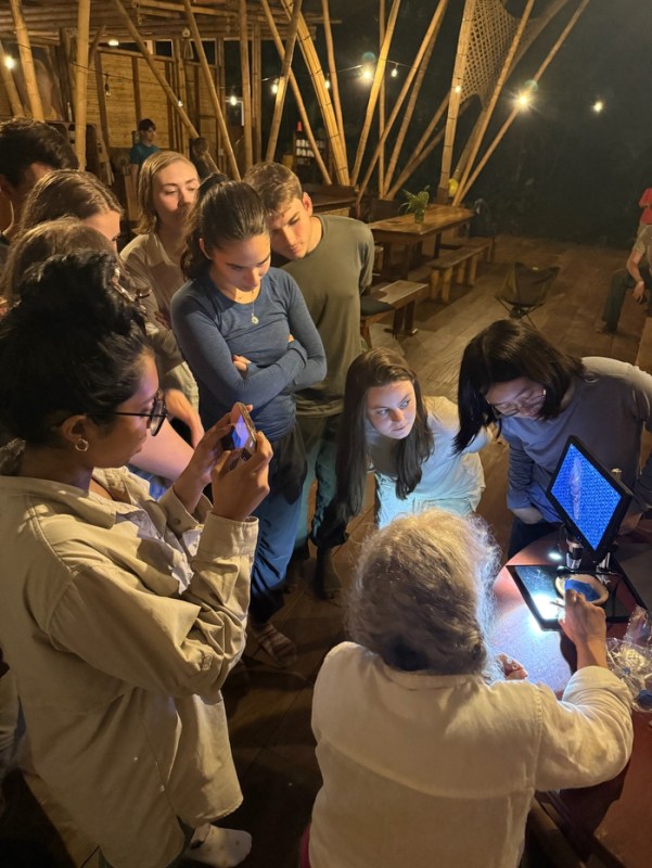 A group of people gathered closely in a wooden structure looking at an illuminated screen.