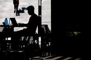 Silhouette of a person sitting at a table typing on a laptop.