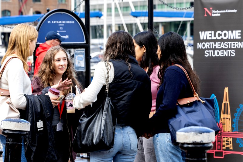 A group of five female students shown chatting in front of a Northeastern London welcome sign.